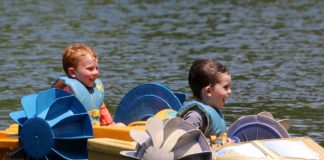Two children in paddleboats on a lake.