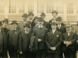 Black and white photo of men in suits and hats standing in front of a building