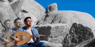 Yoni Avi Battat sitting on rocks with a stringed instrument