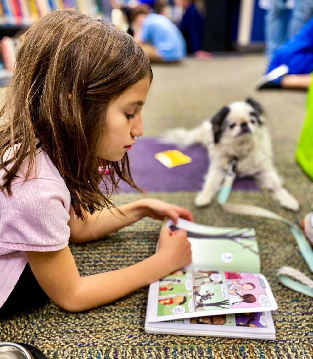 A child reads to a dog through the Mitzvah Mutts program