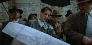 Photo of a man looking down at a long scroll of white paper in a movie set based in Nazi Germany.