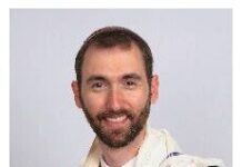 What Is ‘Chanukah’? Headshot of a man with a brown beard and mustache and close-cropped brown hair. He is wearing a striped white sweater over a white shirt and blue tie.