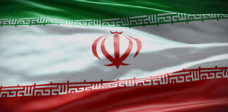 Photo of an Iranian flag: from top to bottom, horizontal stripes of green, white and red with a red tulip-shaped emblem in the center, against the white stripe.