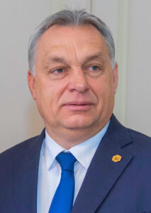 A man with gray hair wearing a jacket with a blue tie.