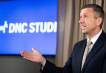 DNC Committee Rejects Resolution Condemning Pro-Israel Lobby AIPAC Specifically A man wearing a jacket and tie and standing in front of a screen.