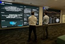 Steven Fransblow, left, and Adam Katz, right, look at the real-time dashboard at the Blue Square Alliance Against Hate command center in Foxborough, Massachusetts.