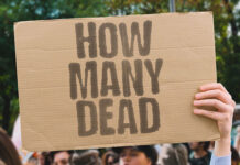 Person holding up a sign that says "How Many Dead"